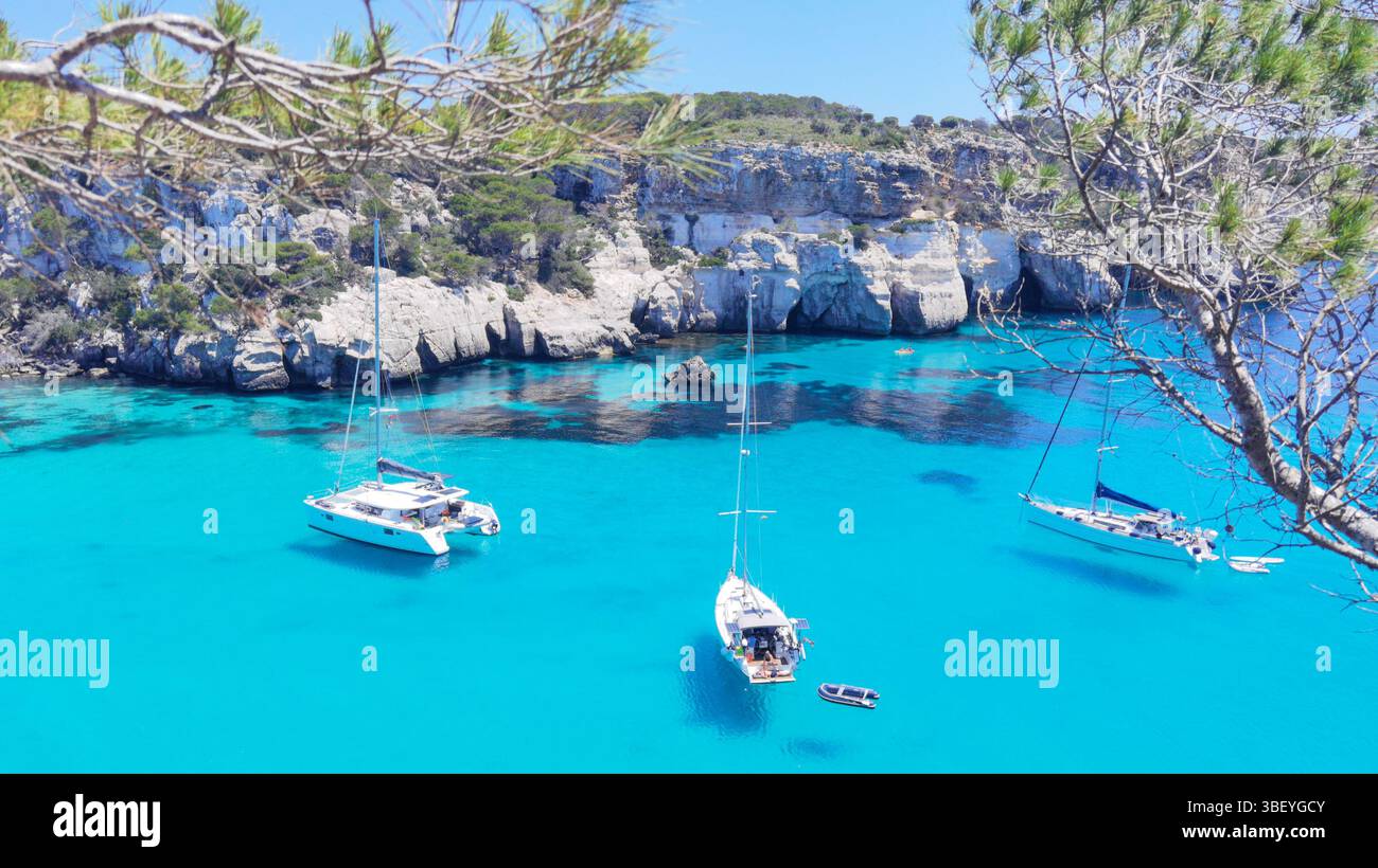 Cala Macarella, türkisfarbenes Wasser, transparentes Meer, schwimmende Yachten, Kiefern, Balearen, Menorca Strand, Mittelmeerküste, kristallklares Wasser - Smartphone-aufgenommenes Stockfoto