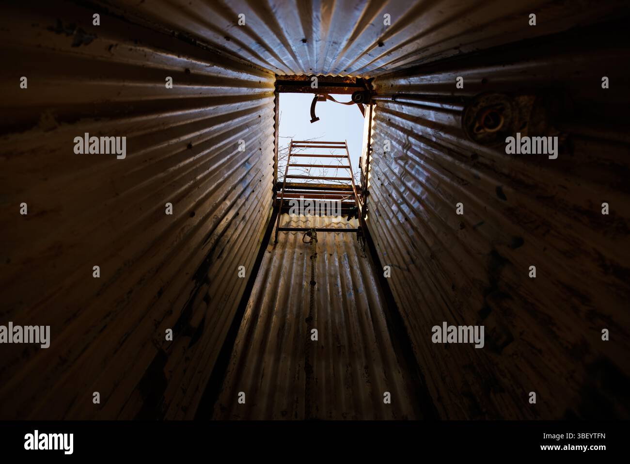 Blick durch einen dunklen Welltunnel in Richtung einer Öffnung mit Leiter und Tageslicht, was eine dramatische Fluchtmöglichkeit oder Industrieszene schafft. Stockfoto