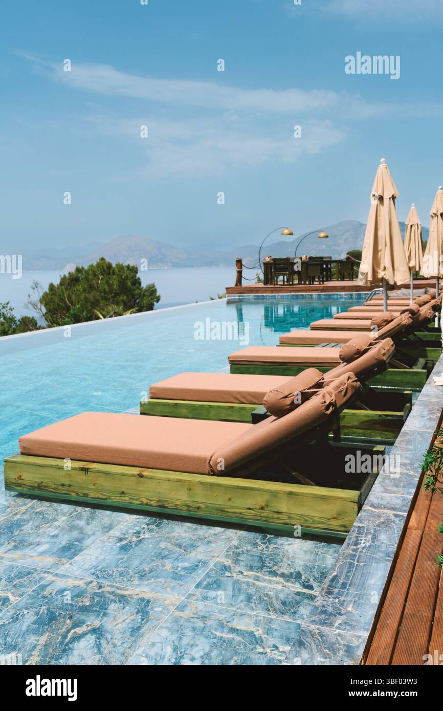 Tagsüber ein Foto vom gemeinsamen Infinity-Pool eines Hotels mit Liegestühlen während der Sommersaison, das luxuriöse Entspannung bietet. Stockfoto