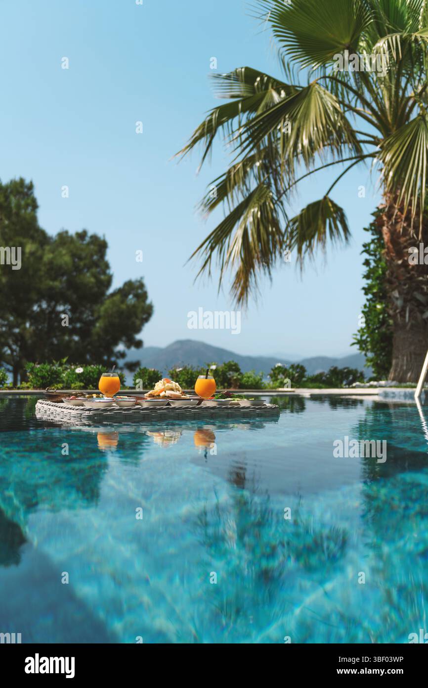 Ein üppiges schwimmendes Frühstück, das wunderschön in einem Swimmingpool serviert wird, mit frischem Obst, Gebäck und Erfrischungen. Stockfoto