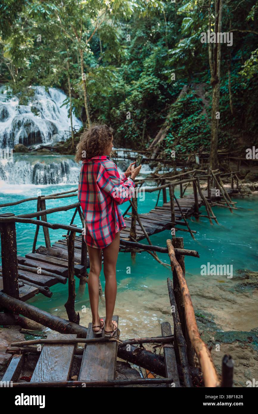 Attraktive Frau fotografiert am Telefon auf der Brücke am Wasserfall in Luwuk, Sulawesi, Indonesien Stockfoto