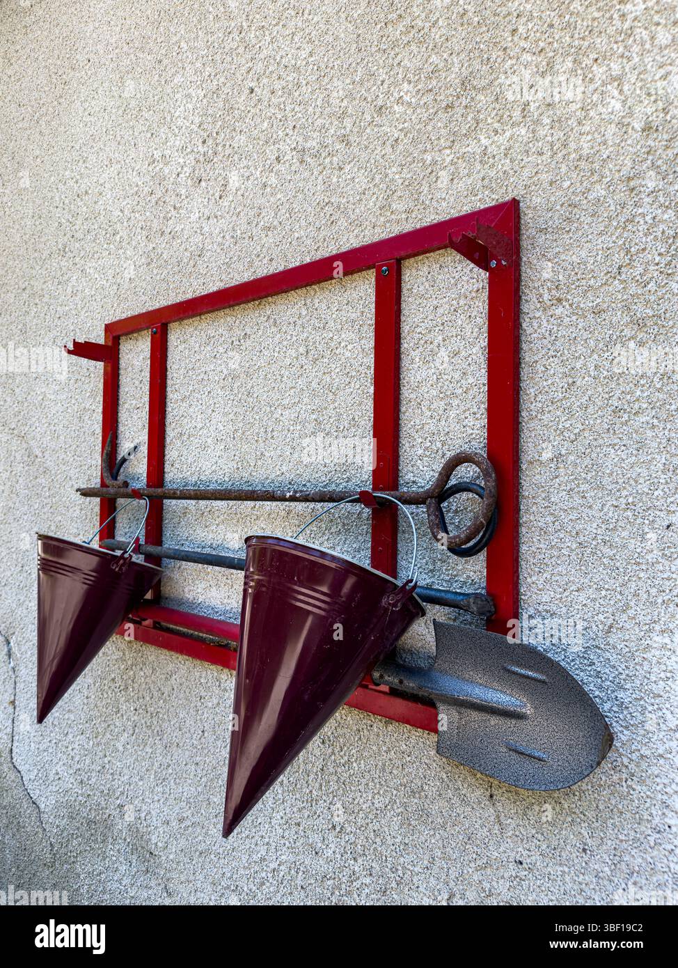 Brandbekämpfungsset an der Wand mit rotem Metallgestell, konischen Eimern, Schaufel und Haken, schräg, strukturierte Oberfläche, Sicherheits- und Notfallausrüstung. Stockfoto