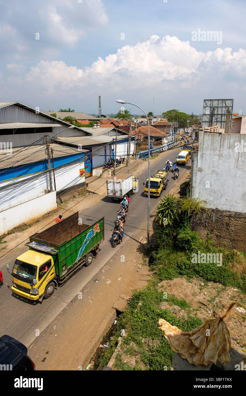 Der Verkehr fließt durch eine stark befahrene Straße in Indonesien, wobei Lastwagen und Motorräder auf der Straße navigieren. Stockfoto