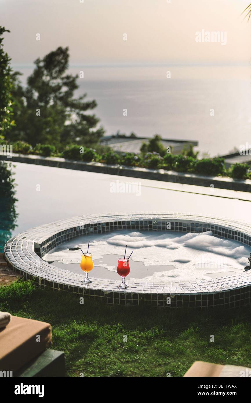 Zwei lebhafte Cocktails oder Obstgetränke neben einem Whirlpool in einem luxuriösen Hotelzimmer am Pool. Stockfoto