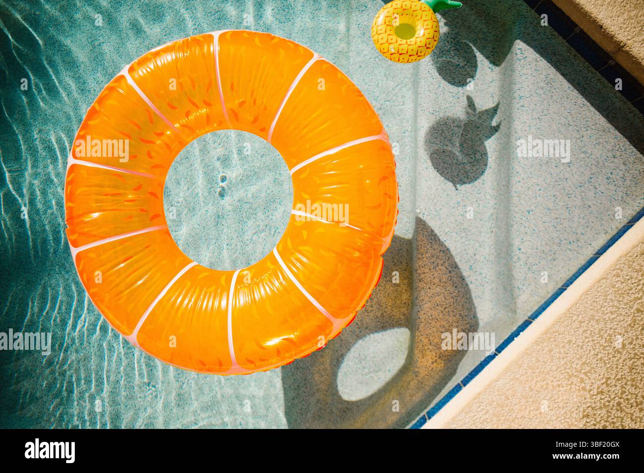 Orangener Pool, Schwimmer und Ananasbecher in einem sonnendurchfluteten Swimmingpool Stockfoto