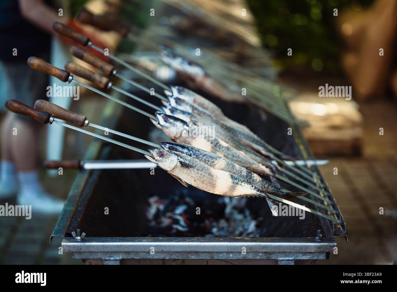 So genannte Steckerlfische - Fisch auf Metallspießen - werden bei einem Festival in Bayern über Holzkohle gegrillt und mit Marinade beschichtet Stockfoto