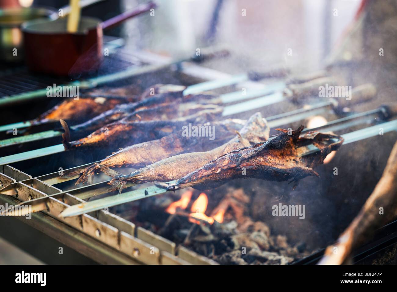 So genannte Steckerlfische - Fisch auf Metallspießen - werden bei einem Festival in Bayern über Holzkohle gegrillt und mit Marinade beschichtet Stockfoto