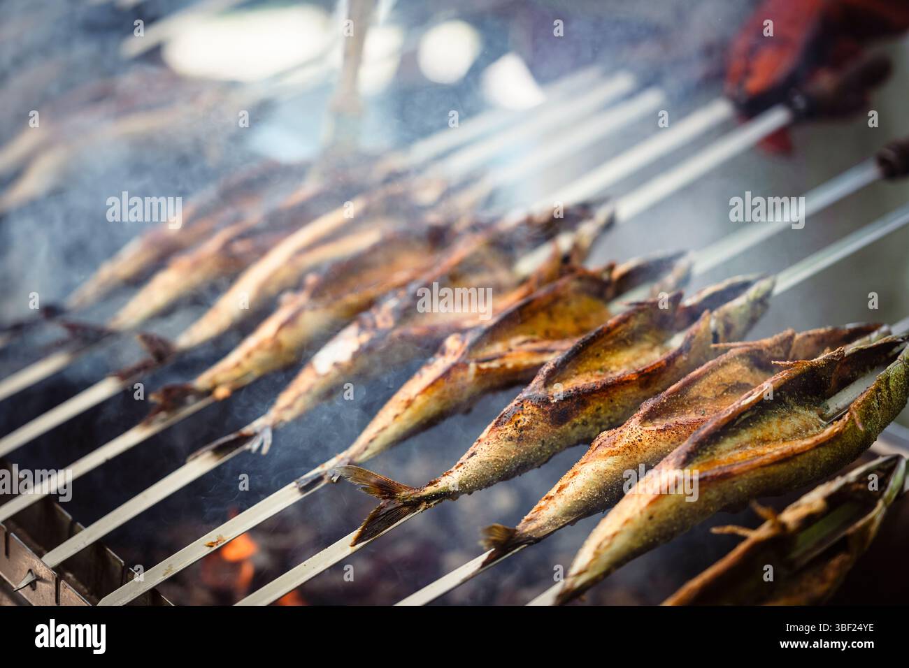 So genannte Steckerlfische - Fisch auf Metallspießen - werden bei einem Festival in Bayern über Holzkohle gegrillt und mit Marinade beschichtet Stockfoto