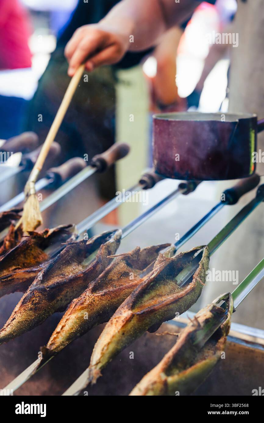 So genannte Steckerlfische - Fisch auf Metallspießen - werden bei einem Festival in Bayern über Holzkohle gegrillt und mit Marinade beschichtet Stockfoto