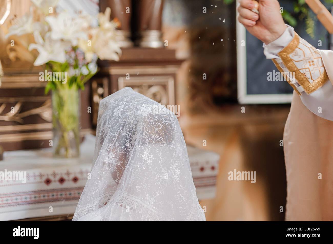 Nahaufnahme einer Braut mit einem Spitzenschleier, die während einer religiösen Hochzeitszeremonie in einer kirchlichen Umgebung einen Segen von einem Priester erhält, der den Glauben symbolisiert Stockfoto