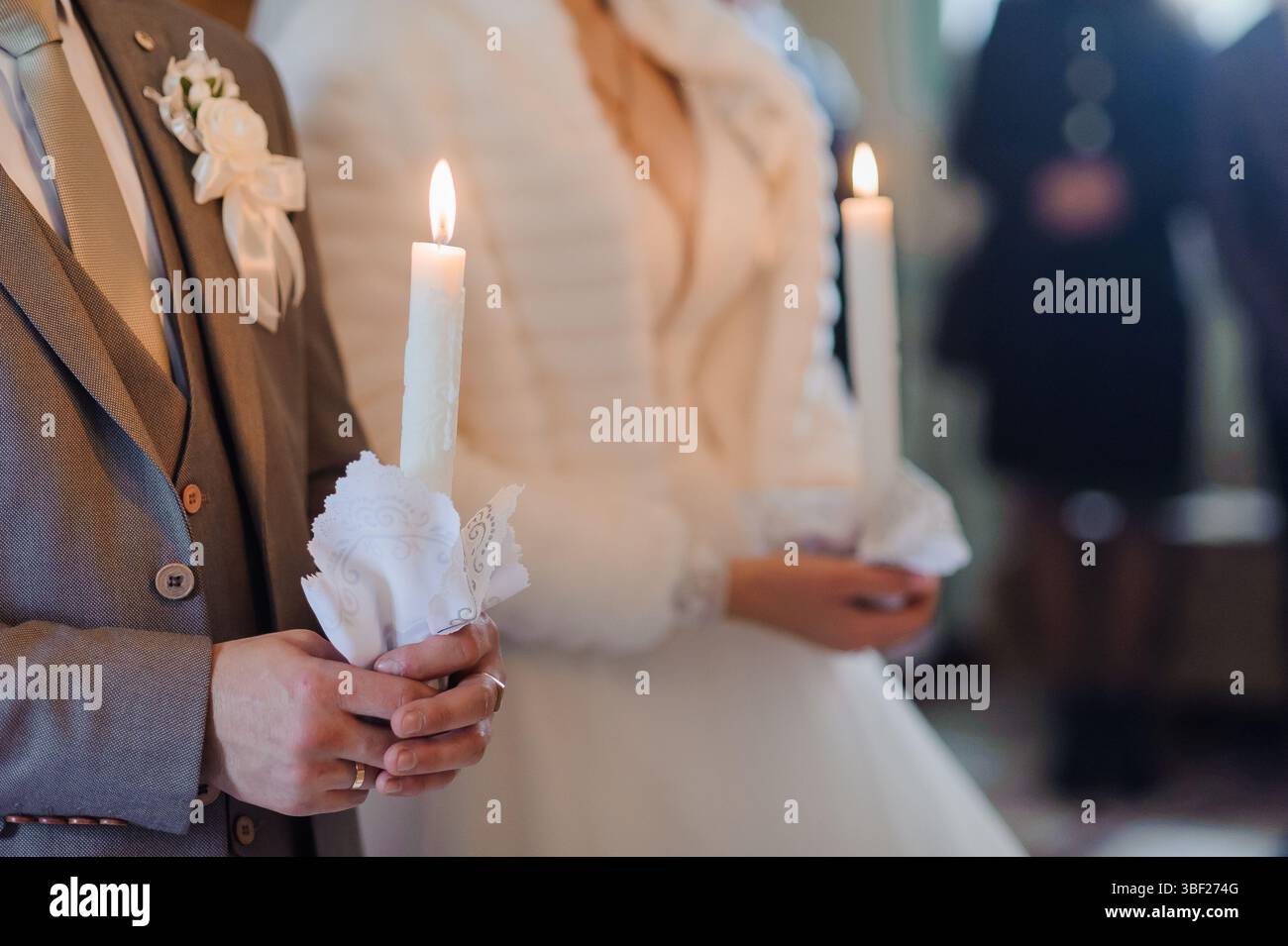 Eine zärtliche Szene während einer Hochzeit, in der ein Bräutigam und eine Braut zündete Kerzen und weiße Spitzen-Taschentücher greifen und die Einheit und den Glauben innerhalb einer Kirche symbolisieren Stockfoto