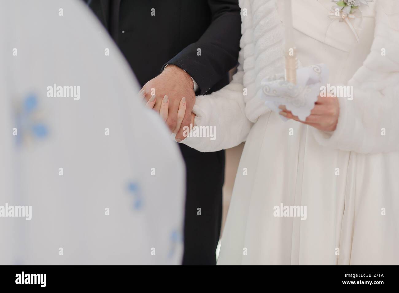 Eine Nahaufnahme einer Hochzeitszeremonie zeigt einen Bräutigam in einem dunklen Anzug und eine Braut in einem weißen Kleid, deren Hände zusammengeschlossen sind und die Liebe symbolisieren Stockfoto
