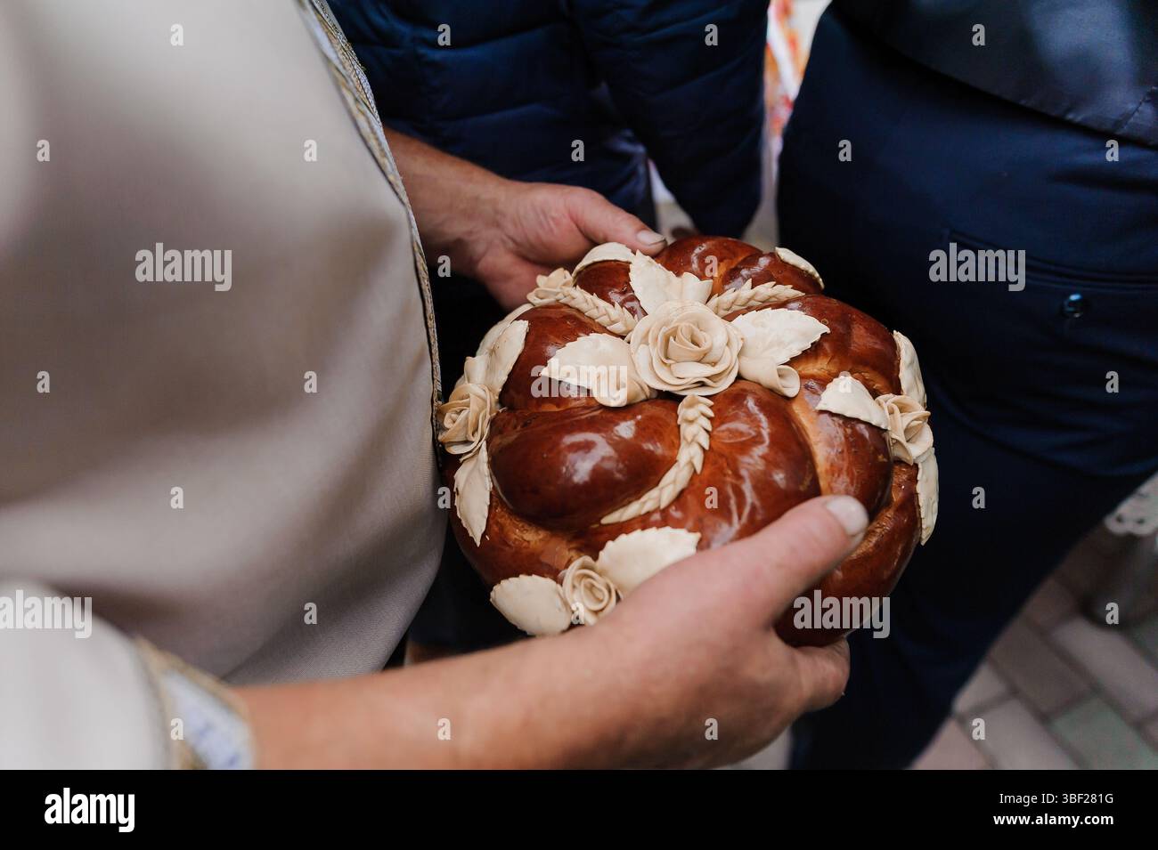 Eine Nahaufnahme, die den Moment feststellt, in dem eine Braut und ein Bräutigam ein wunderschön dekoriertes polnisches Korowaj-Brot halten, das mit komplizierten Weizenmotiven und Del verziert ist Stockfoto