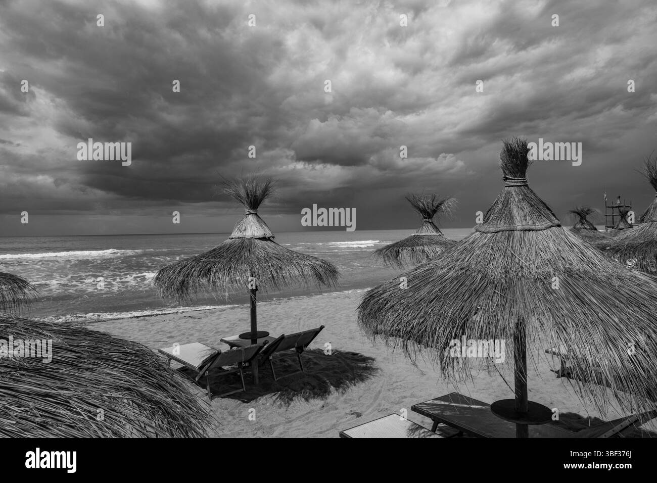 Küste mit dunklen Wolken und Strohschirmen in der Toskana, Italien Stockfoto