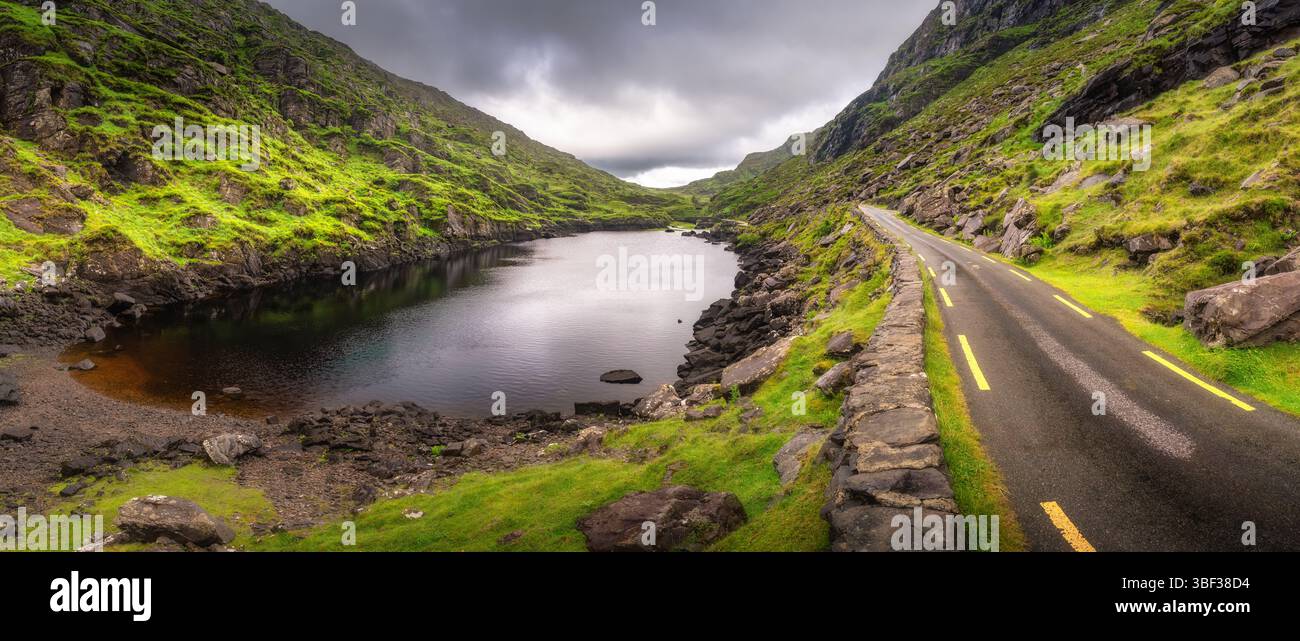 Eine atemberaubende Aussicht zeigt eine gewundene Straße, die anmutig am Rand eines ruhigen Sees liegt, wunderschön eingebettet zwischen üppigen grünen Hügeln von Gap of Dunl Stockfoto
