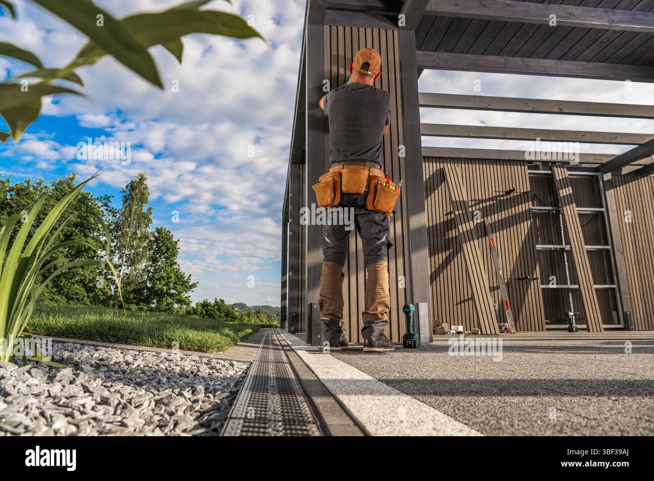 Ein Bauarbeiter konzentriert sich auf die Befestigung von Holzplatten an einer eleganten Außenstruktur. Stockfoto