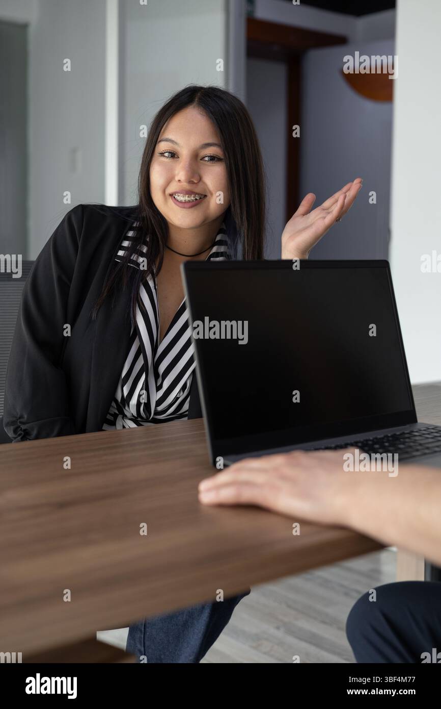 Eine junge Frau lächelt leise mit einem ruhigen Ausdruck in einer Büroumgebung. Dieses warme Bild vermittelt Positivität, Selbstvertrauen und Frieden, perfekt für uns Stockfoto