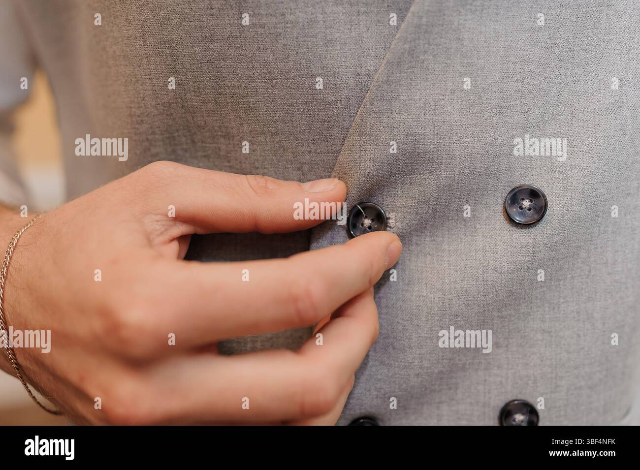 Eine Nahaufnahme zeigt einen Mann, der elegant die Knöpfe einer grauen Tweed-Weste anschließt und das strukturierte Material und die raffinierten Details des Su betont Stockfoto