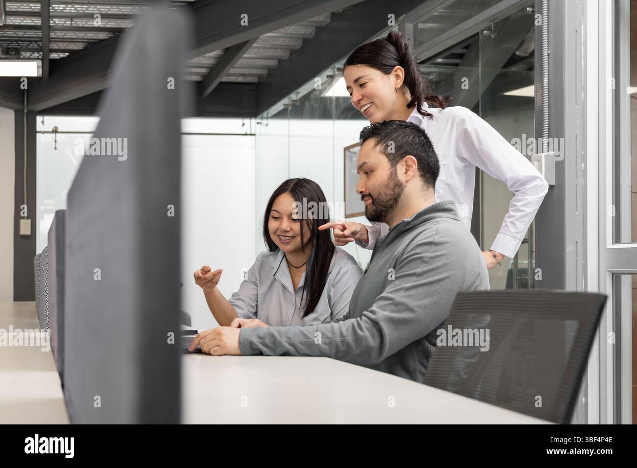 Kollegen konzentrieren sich auf den Bildschirm, während sie den neuesten Verkaufsbericht analysieren und in einer modernen, offenen Büroumgebung zusammenarbeiten. Stockfoto