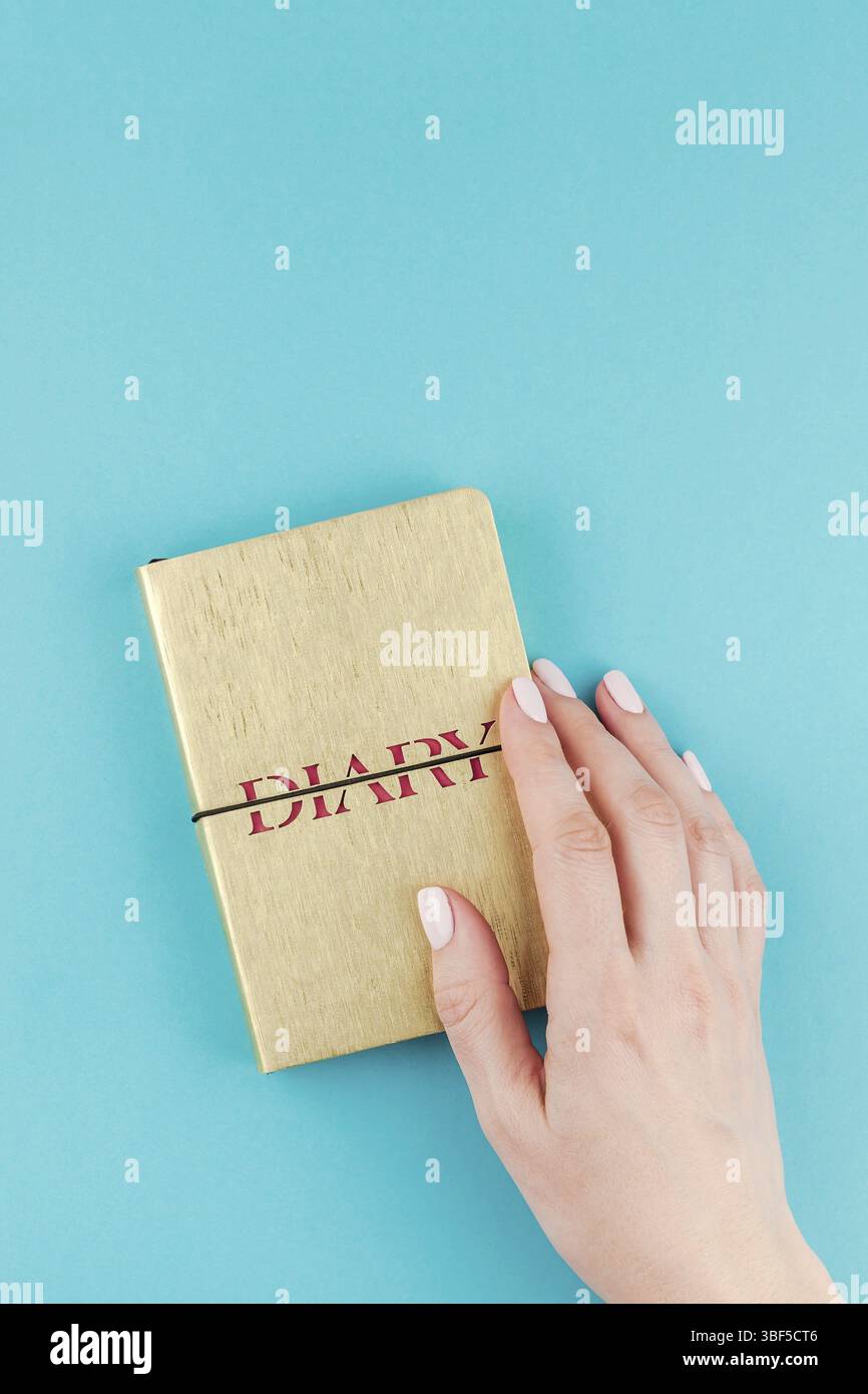 Kreative Flach von Frau Hände, die kleine goldene Notizbuch Tagebuch mit Kopie Speicherplatz auf Türkis Papier Hintergrund in minimalistischem Stil. Vorlage für f Stockfoto