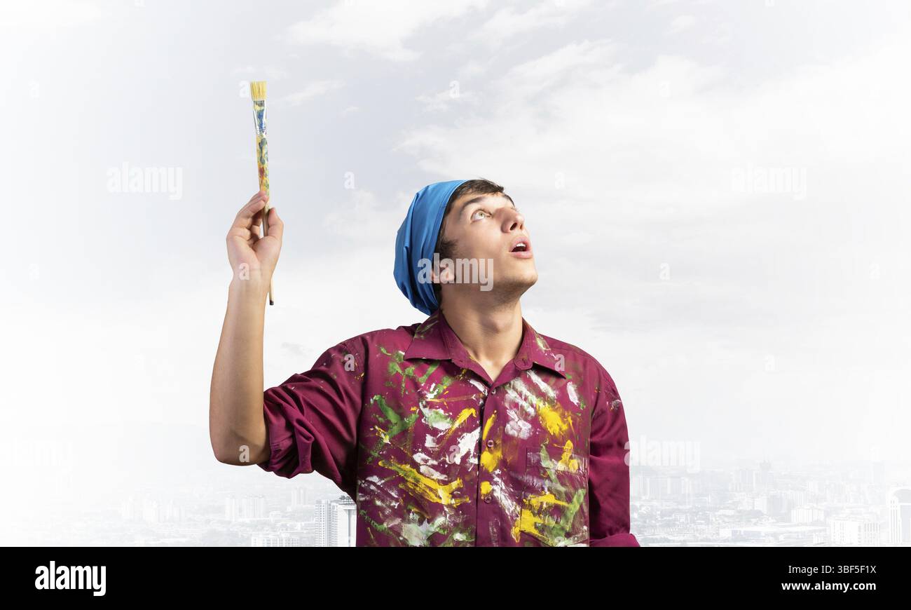 Junge Maler Künstler holding Pinsel Overhead. Portrait von Decorator nach oben auf und blauer Himmel. Künstlerischen Besetzung und kreative Prof Stockfoto
