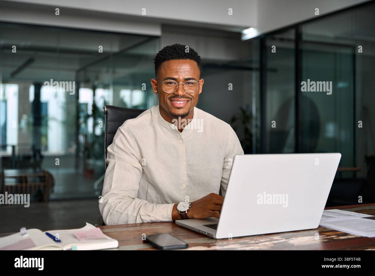 Glücklicher professioneller afrikanischer Geschäftsmann, der bei der Arbeit auf die Kamera schaut, Porträt. Stockfoto