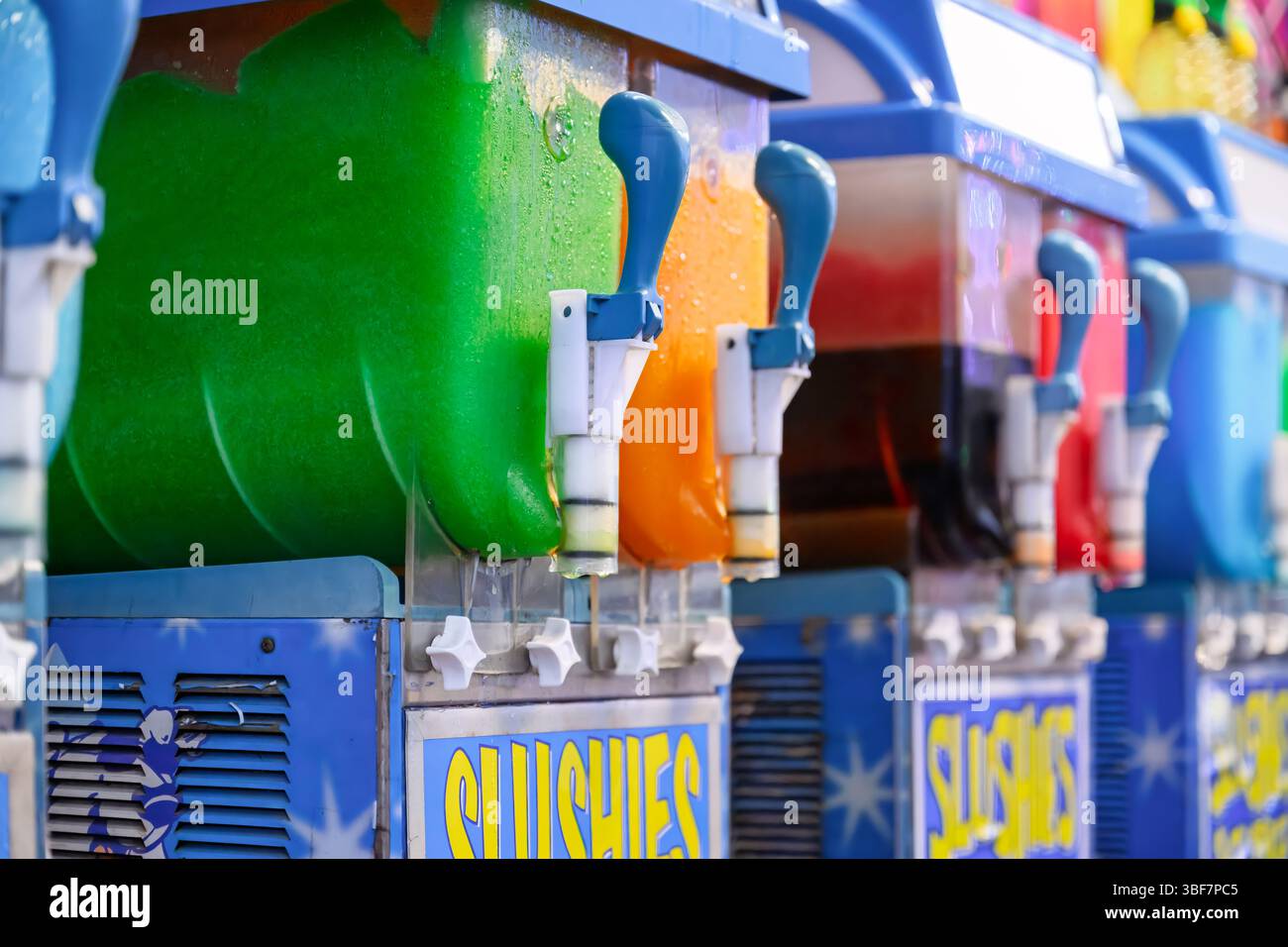 Kommerzielle Slushie-Maschinen am Karneval mit farbenfrohen grünen und orangen Tiefkühlgetränken Stockfoto