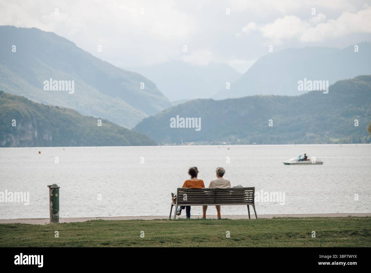 Zwei Frauen saßen auf einer Bank in einem Park in Annecy am Rande der französischen Alpen, mit Blick auf das Wasser des Sees und die wunderschönen Berge. Stockfoto