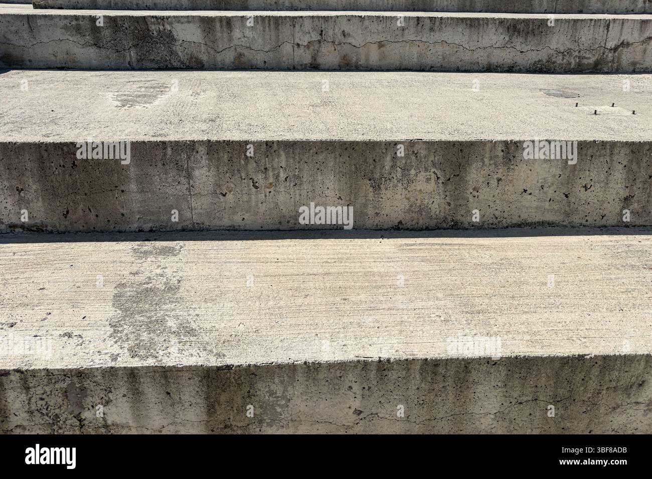 Betontreppen in Nahaufnahme mit rauer Oberfläche, Rissen, Flecken, horizontalem Muster, Tageslicht, abstraktem architektonischem Hintergrund für Design oder Konstruktion Stockfoto