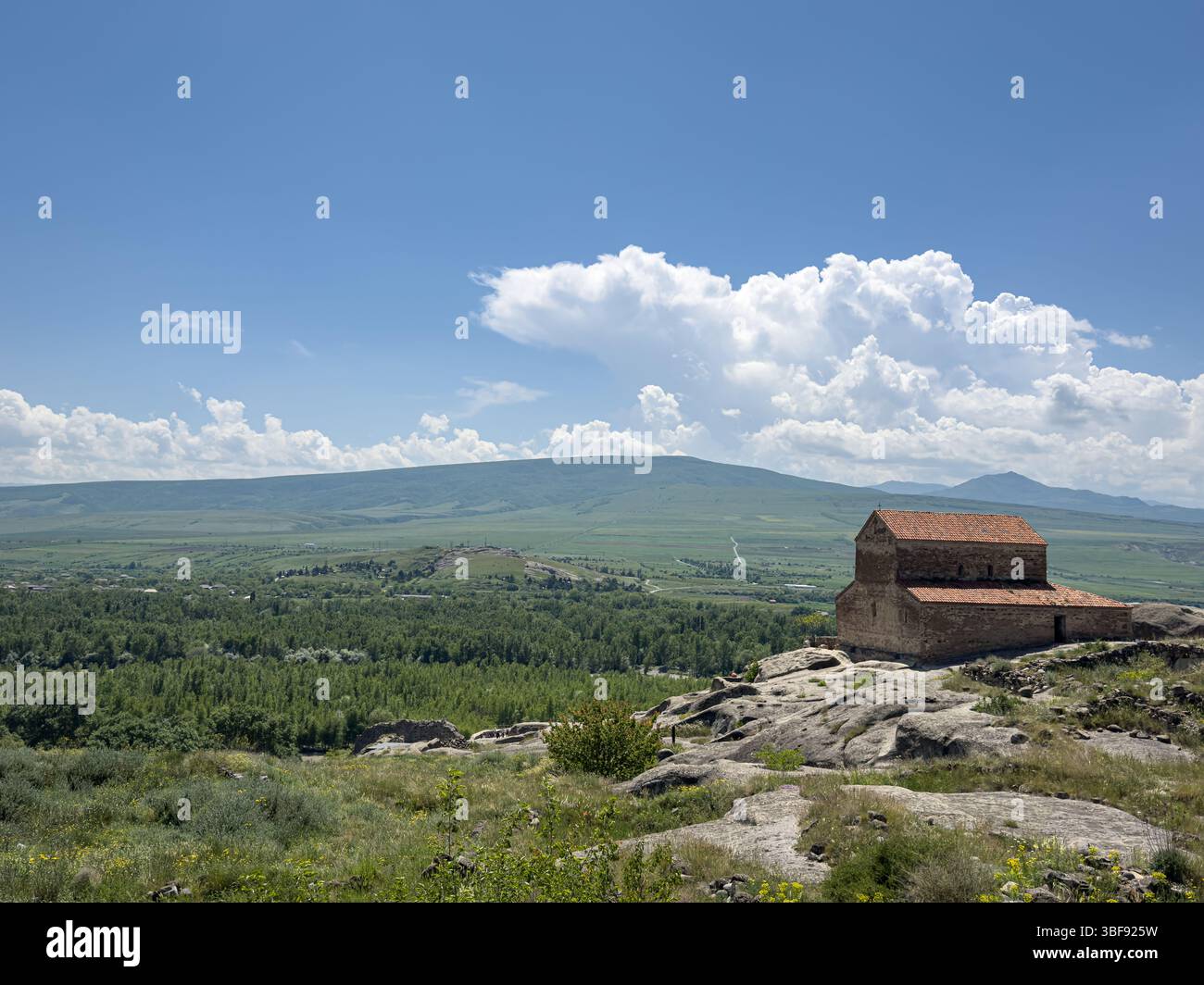 Panoramablick auf die alte Höhlenstadt Uplistsikhe und die Kirche Uplistsikhe in Georgia, mit grünem Tal und Bergen unter blauem Himmel. Stockfoto