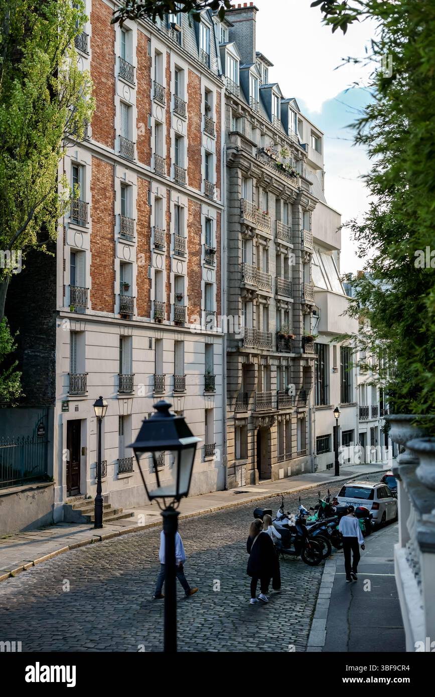 Ein etwas breiterer Blick auf dieselbe Pariser Straße, wo mehr Fußgänger entlang der Kopfsteinpflasterstraße neben den traditionellen Gebäuden und PA laufen Stockfoto