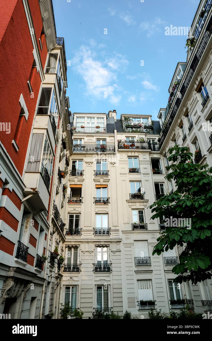 Blick direkt von einem Innenhof auf die umliegenden hohen, klassischen Pariser Apartmenthäuser mit zahlreichen Fenstern und Balkonen gegen ein Blau Stockfoto