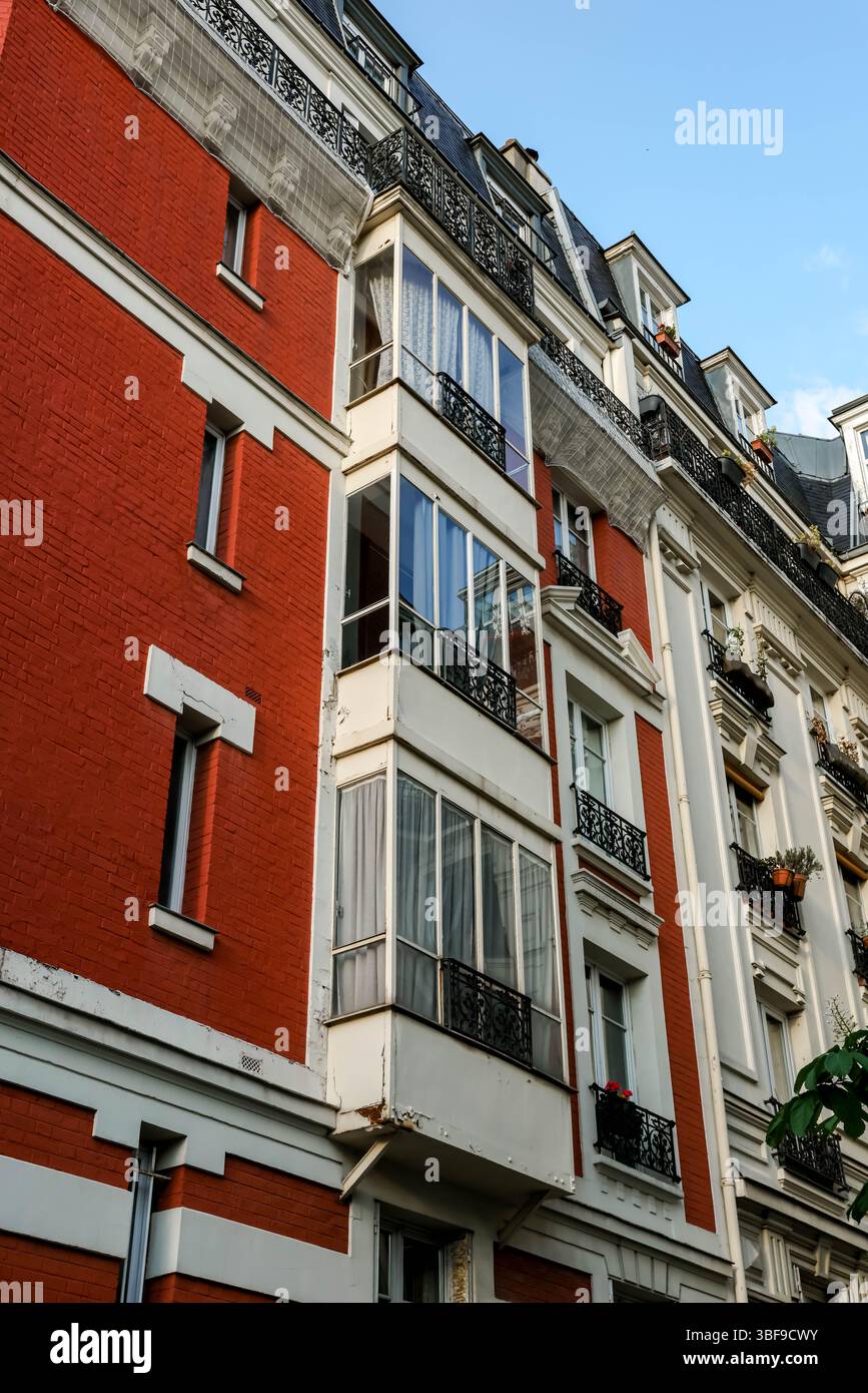 Ein abgewinkelter Blick auf die Fassade eines Pariser Gebäudes, der einen deutlichen Kontrast zwischen einem Abschnitt mit rotem Mauerwerk und einem anderen mit weißem Stein und Abschlussball zeigt Stockfoto