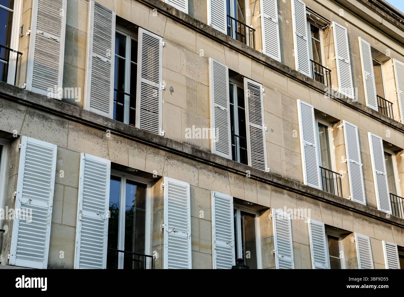 Ein detaillierter Blick auf die oberen Stockwerke eines traditionellen Pariser Steingebäudes, der das sich wiederholende Muster von Fenstern mit klassischen weißen Holzs betont Stockfoto