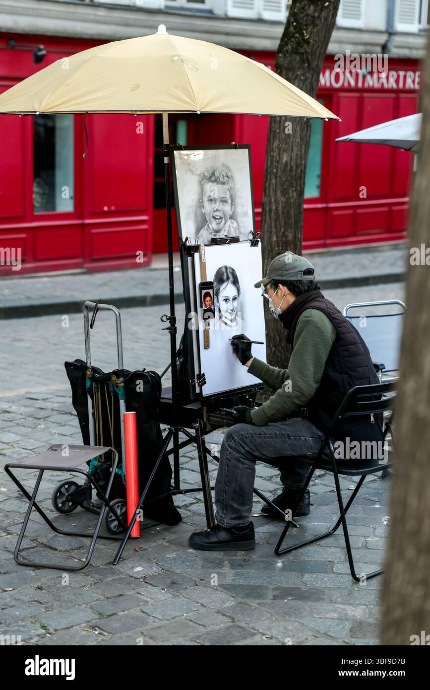 Ein Straßenkünstler, der eine Maske trägt und unter einem großen Schirm sitzt, zeichnet ein Porträt auf einer Staffelei am Place du Tertre, Montmartre, Paris, mit einem roten Bügel Stockfoto