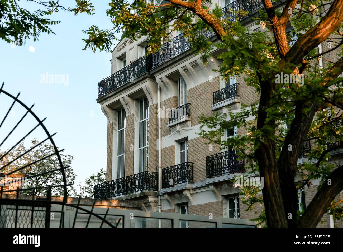 Ein elegantes Pariser Apartmentgebäude mit klassischen architektonischen Details, darunter kunstvoll verzierte schmiedeeiserne Balkone und große Fenster, eingerahmt von Stockfoto