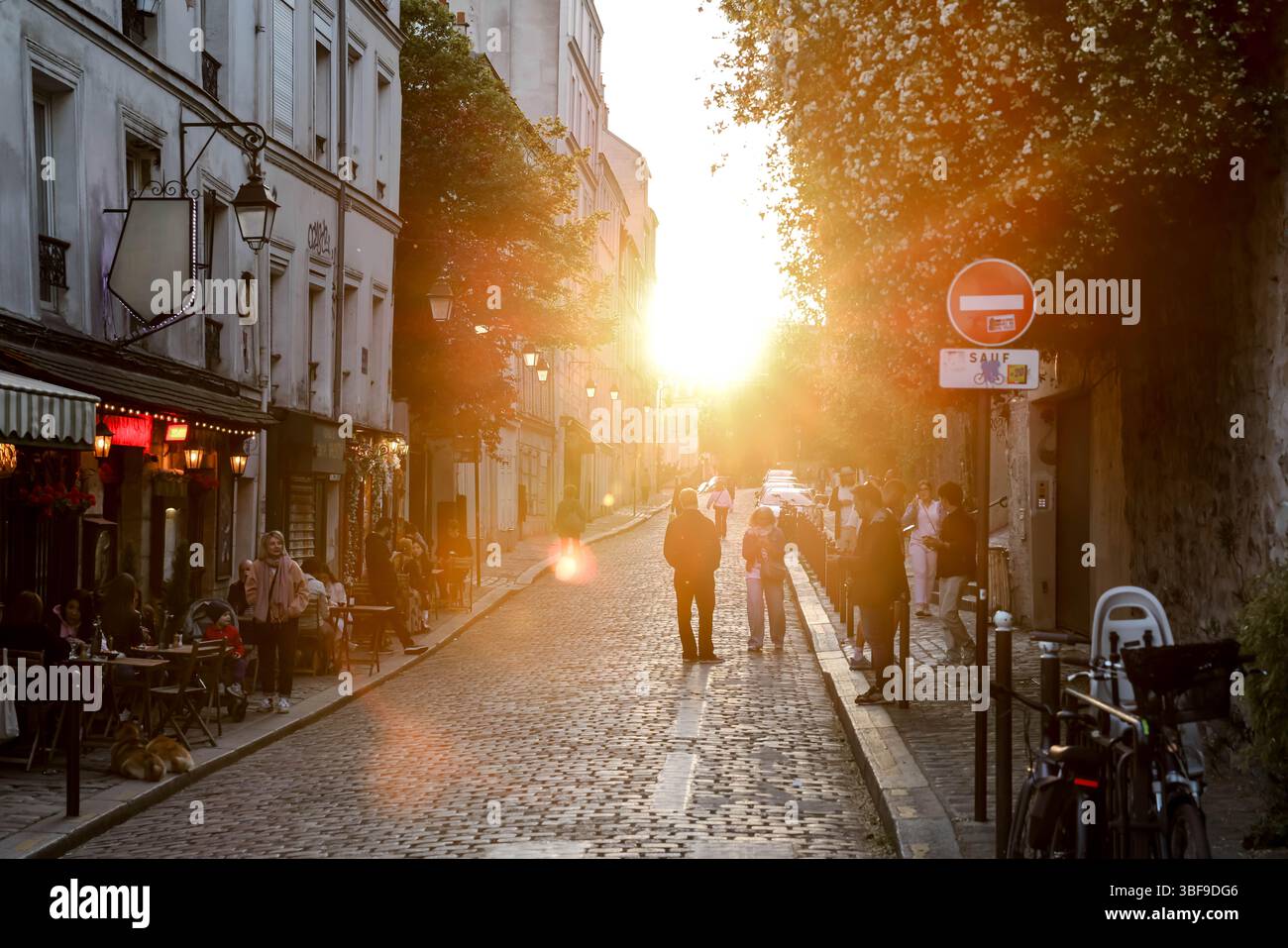 Eine typische Pariser Kopfsteinpflasterstraße wimmelt während der magischen goldenen Stunde von Fußgängern. Warmes Sonnenuntergangslicht beleuchtet das historische Gebäude Stockfoto