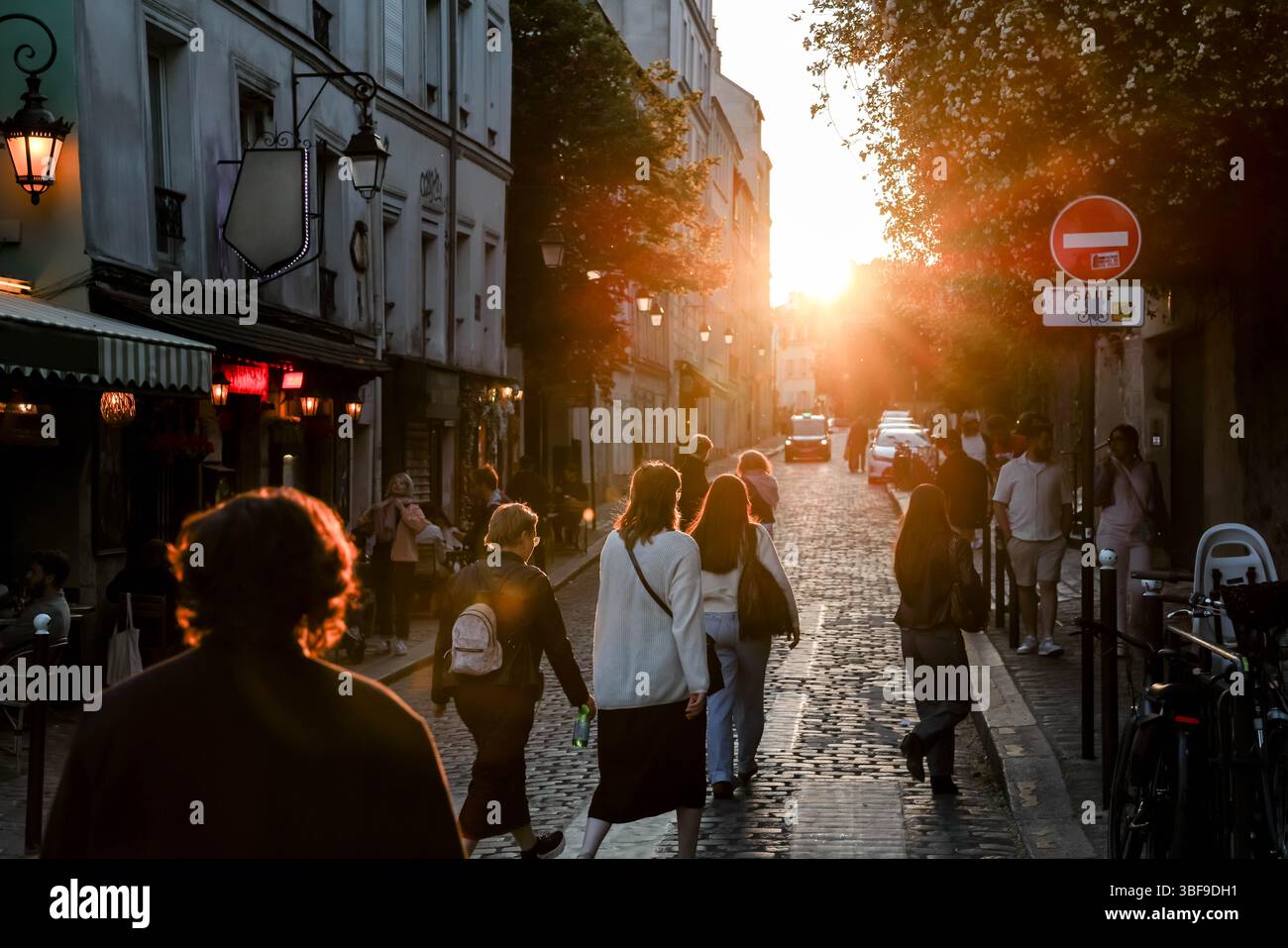 Eine typische Pariser Kopfsteinpflasterstraße wimmelt während der magischen goldenen Stunde von Fußgängern. Warmes Sonnenuntergangslicht beleuchtet das historische Gebäude Stockfoto