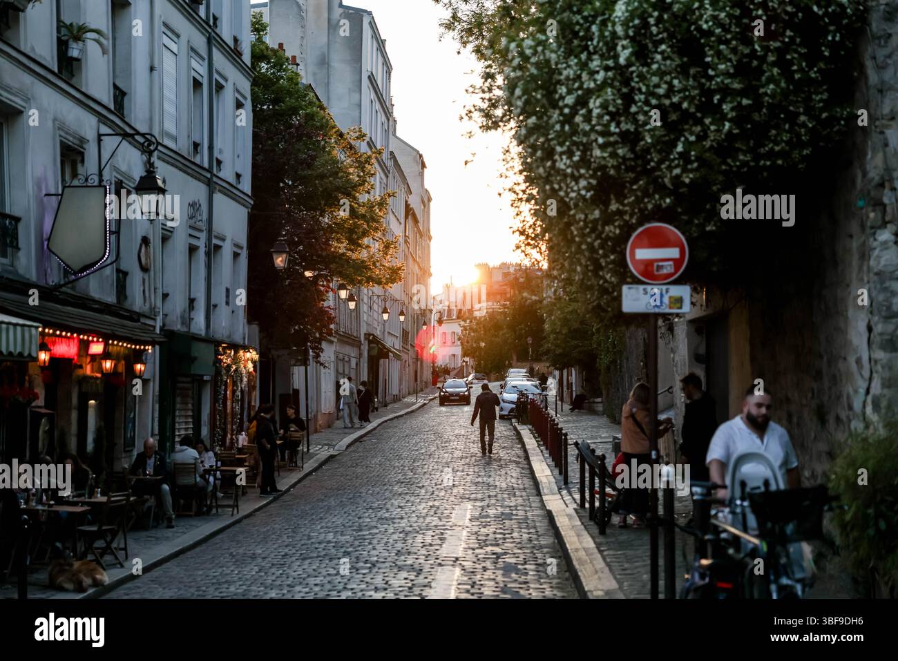 Eine typische Pariser Kopfsteinpflasterstraße wimmelt während der magischen goldenen Stunde von Fußgängern. Warmes Sonnenuntergangslicht beleuchtet das historische Gebäude Stockfoto
