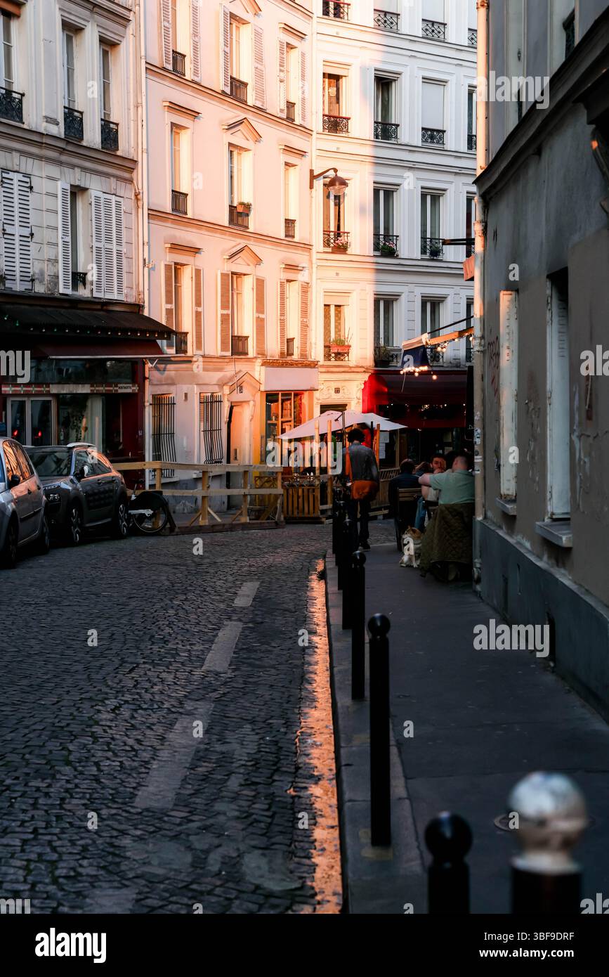 Die eleganten Pariser Gebäudefassaden und eine kopfsteingepflasterte Straße werden wunderschön vom warmen Glanz der goldenen Stunde beleuchtet, was den Klassiker unterstreicht Stockfoto