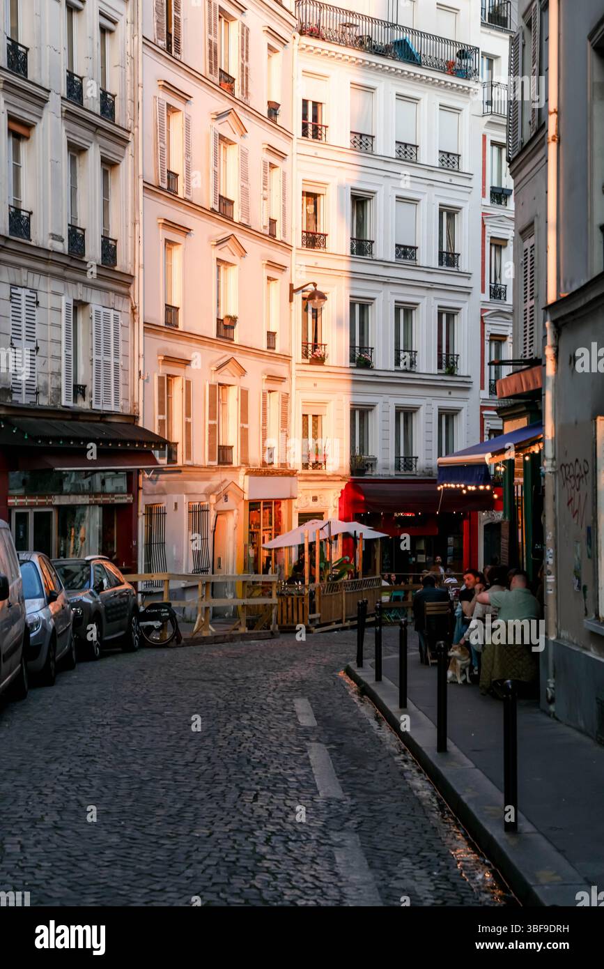 Die eleganten Pariser Gebäudefassaden und eine kopfsteingepflasterte Straße werden wunderschön vom warmen Glanz der goldenen Stunde beleuchtet, was den Klassiker unterstreicht Stockfoto
