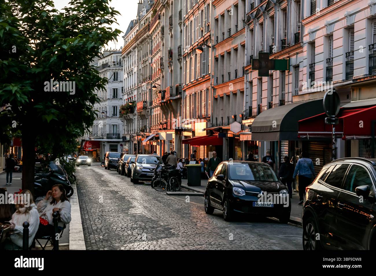 Die belebte Rue des Abbesses in Paris wird am Abend zum Leben erweckt, mit Spaziergängen, Restaurants in Cafés im Freien und Geschäften wie „Fromagerie“. Stockfoto
