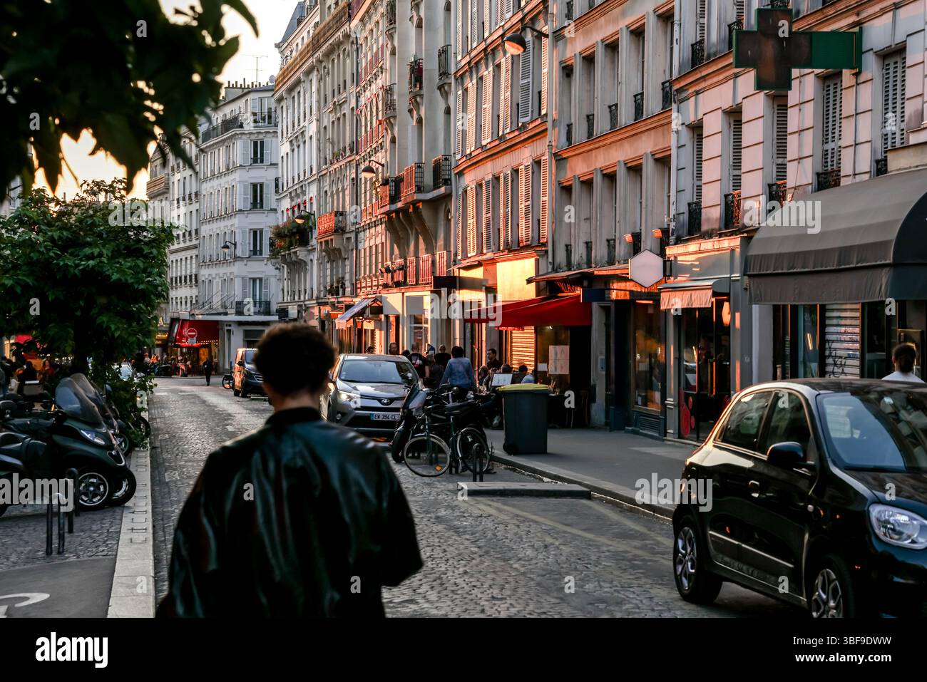 Die belebte Rue des Abbesses in Paris wird am Abend zum Leben erweckt, mit Spaziergängen, Restaurants in Cafés im Freien und Geschäften wie „Fromagerie“. Stockfoto