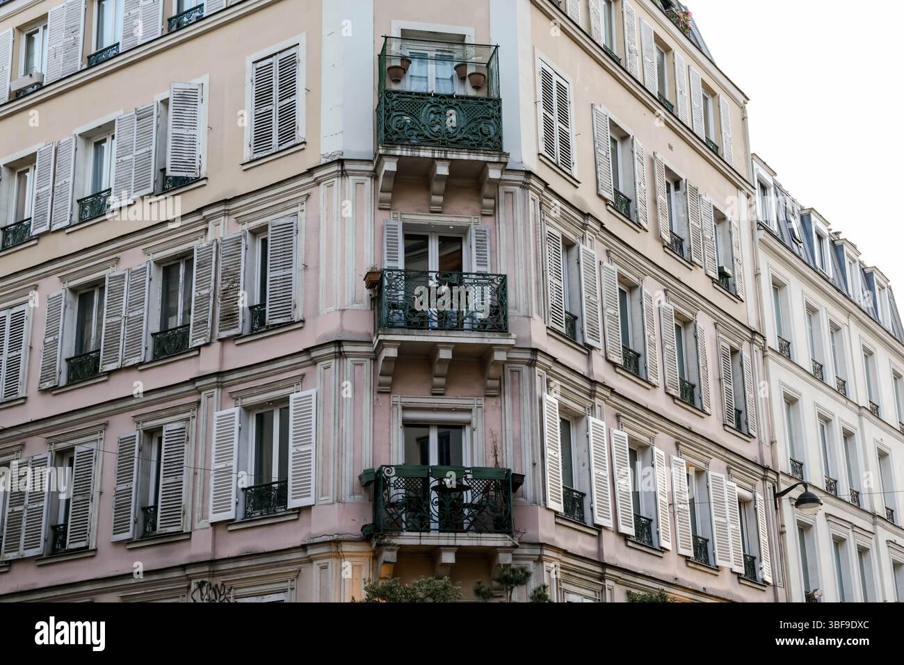 Ein markantes Pariser Eckgebäude fällt mit seiner blassrosa Fassade, den traditionellen weißen Fensterläden und den kontrastierenden, verzierten grünen Schmiedearbeiten ins Auge Stockfoto