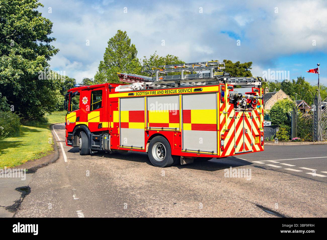 Ein schottisches Feuerwehrauto auf einem Ruf auf einer von Bäumen gesäumten Straße, ausgestattet mit Leitern und Ausrüstung für den Notfall Stockfoto