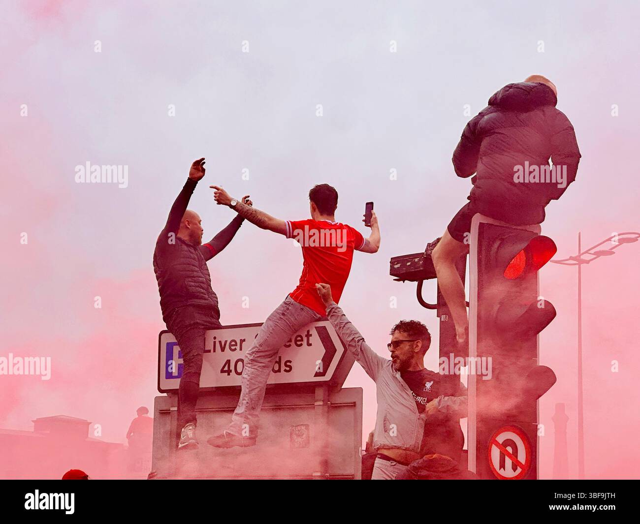 Die Männer feiern an Ampeln und Straßenschildern am Strand, die Arme wurden während der Liverpool-Parade am 25. Mai 2025 in rotem Rauch erhoben - Smartphone-aufgenommenes Stockfoto