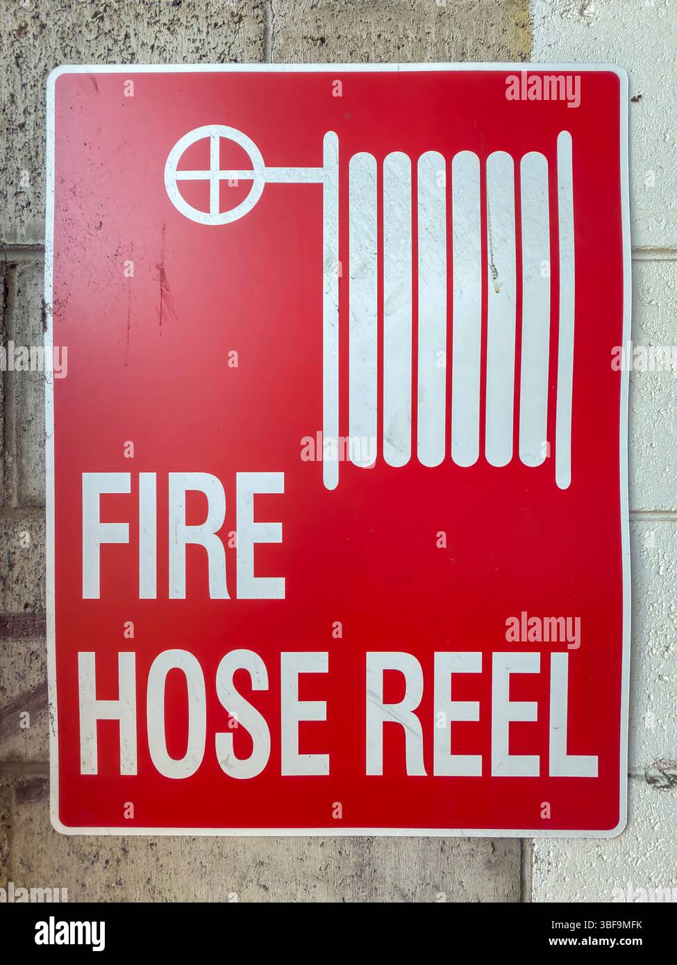 Foto eines alten und schmutzigen roten Metallschlauchschilds auf der Rolle, das sich an einer schmutzigen Wand neben Löschanlagen an einem Industriestandort befindet Stockfoto