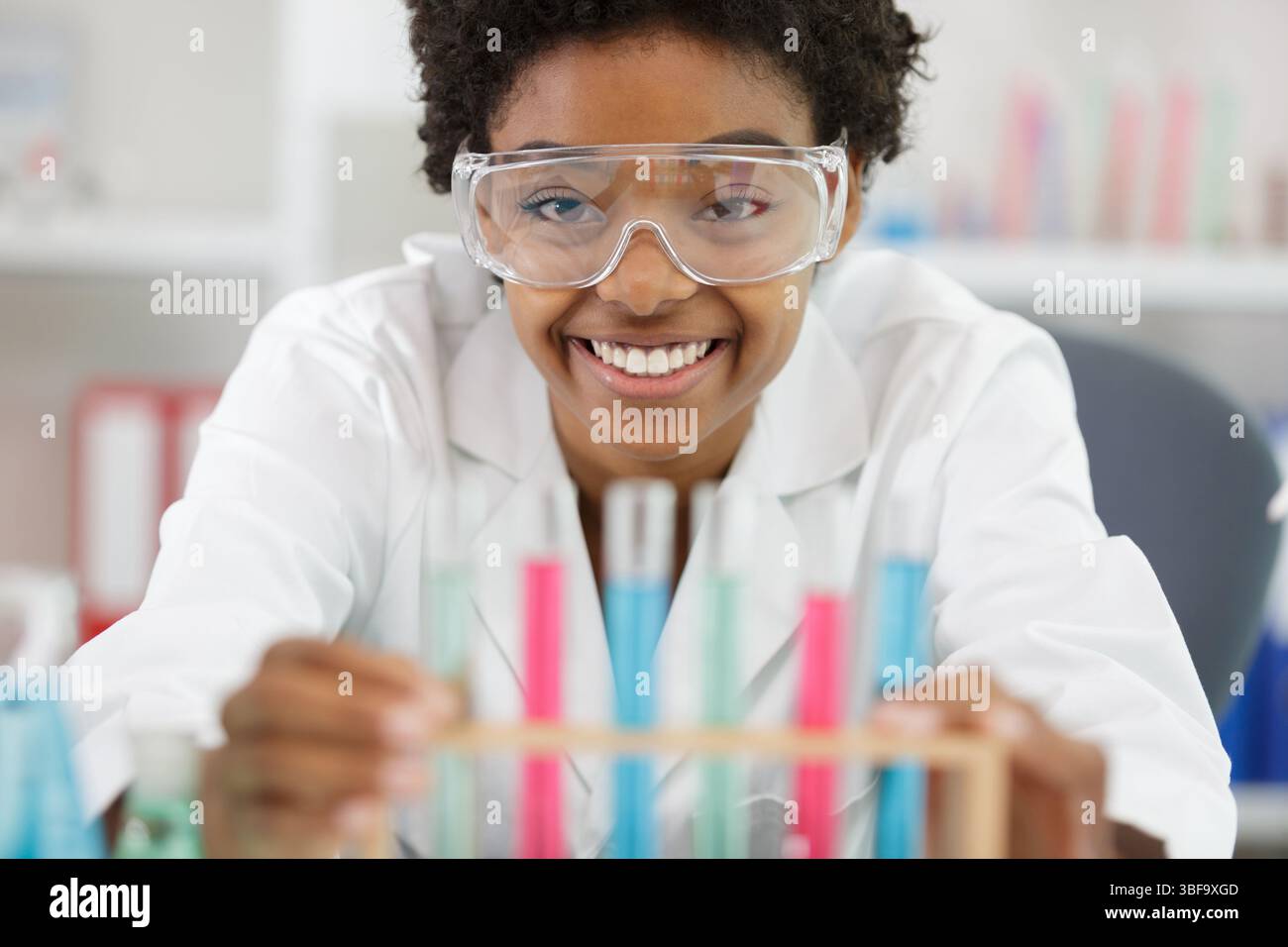 Glückliche Frau mit Brille hält bunte Flüssigkeiten Stockfoto