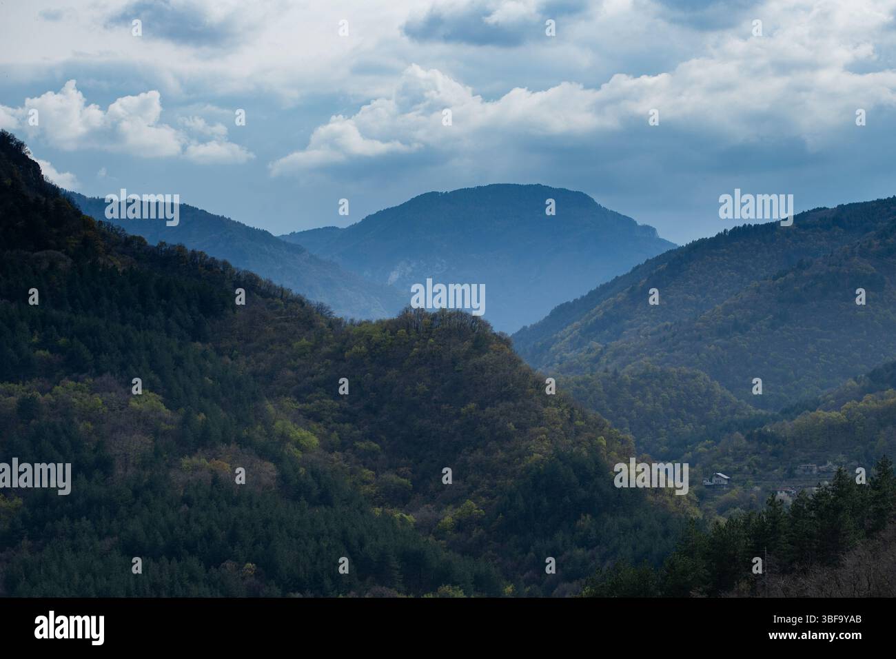 Unter einem Himmel voller schwerer Wolken entfaltet sich eine riesige Reihe bewaldeter Berge in Schichten. Die Szene wird in blaue, atmosphärische Töne eingeblendet Stockfoto