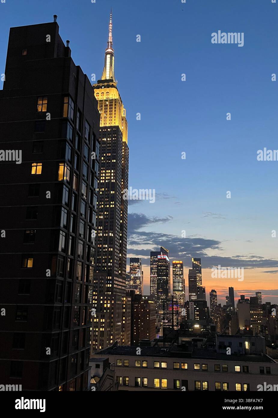 Stadtbild eines klaren Frühlingsabends mit dem beleuchteten Empire State Building im Vordergrund und den Wolkenkratzern von Hudson Yards im Hintergrund, die nach Westen schauen, 2025, NYC, USA - Smartphone-aufgenommenes Stockfoto